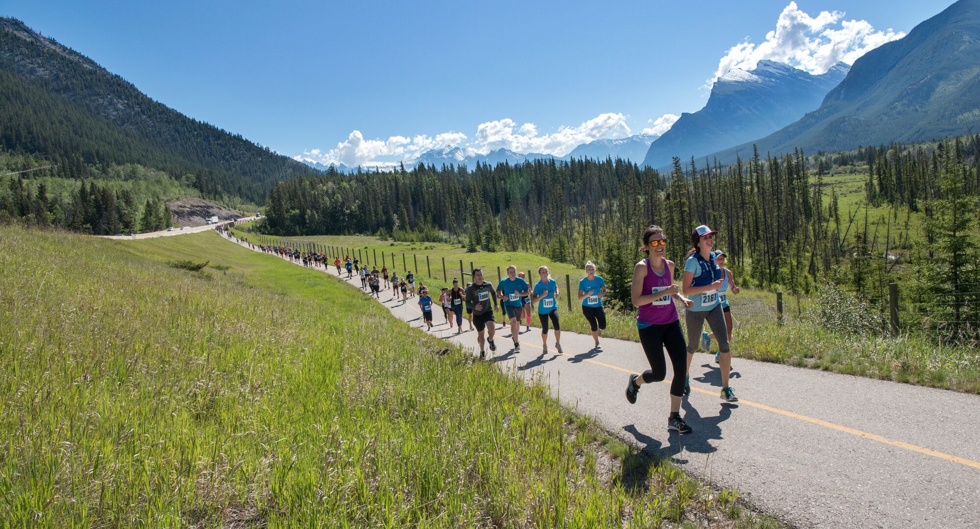 People participating in the Banff Marathon running on a trail with mountains in the background